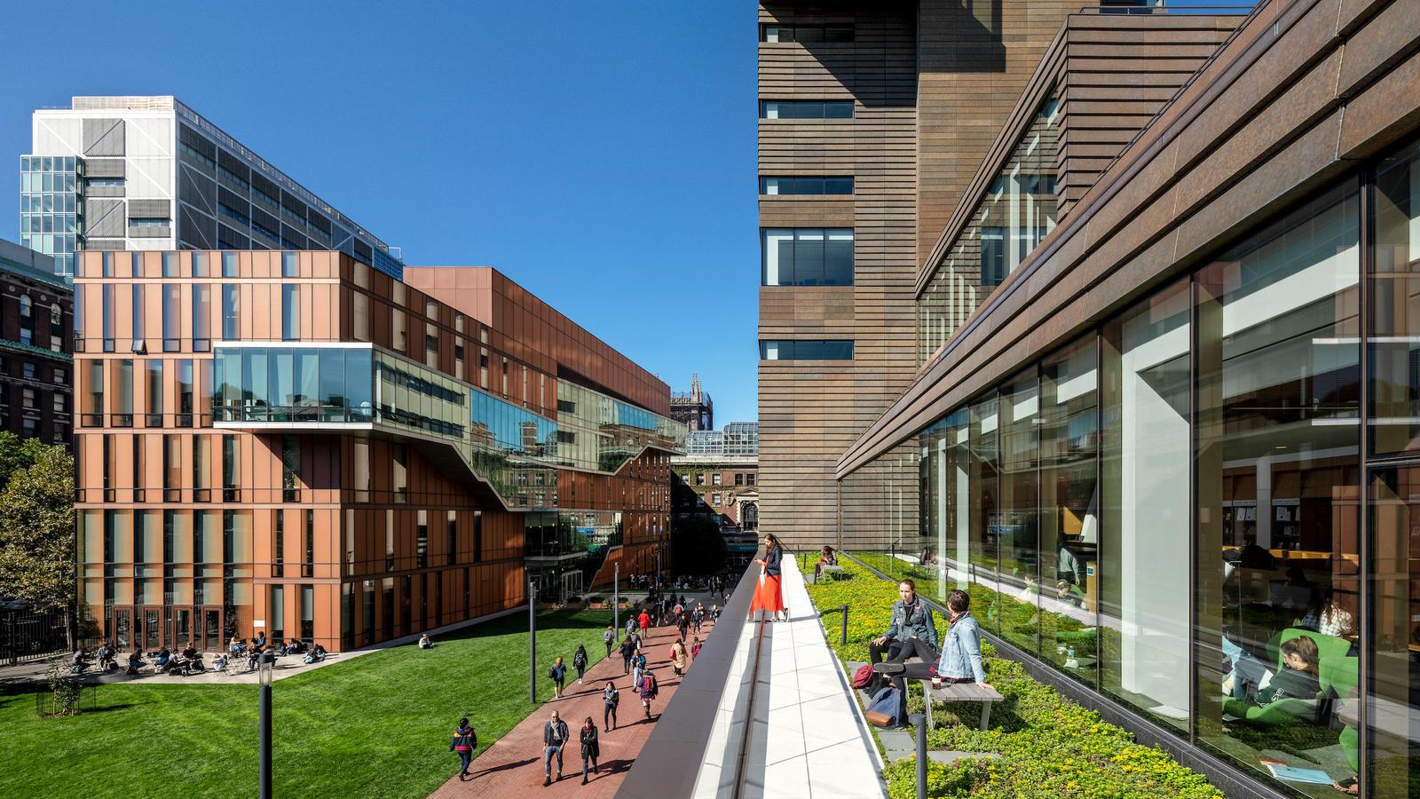 A view of Barnard's campus with students on Milstein's terrace, students walking on the sidewalk, and the Diana Center in the distance